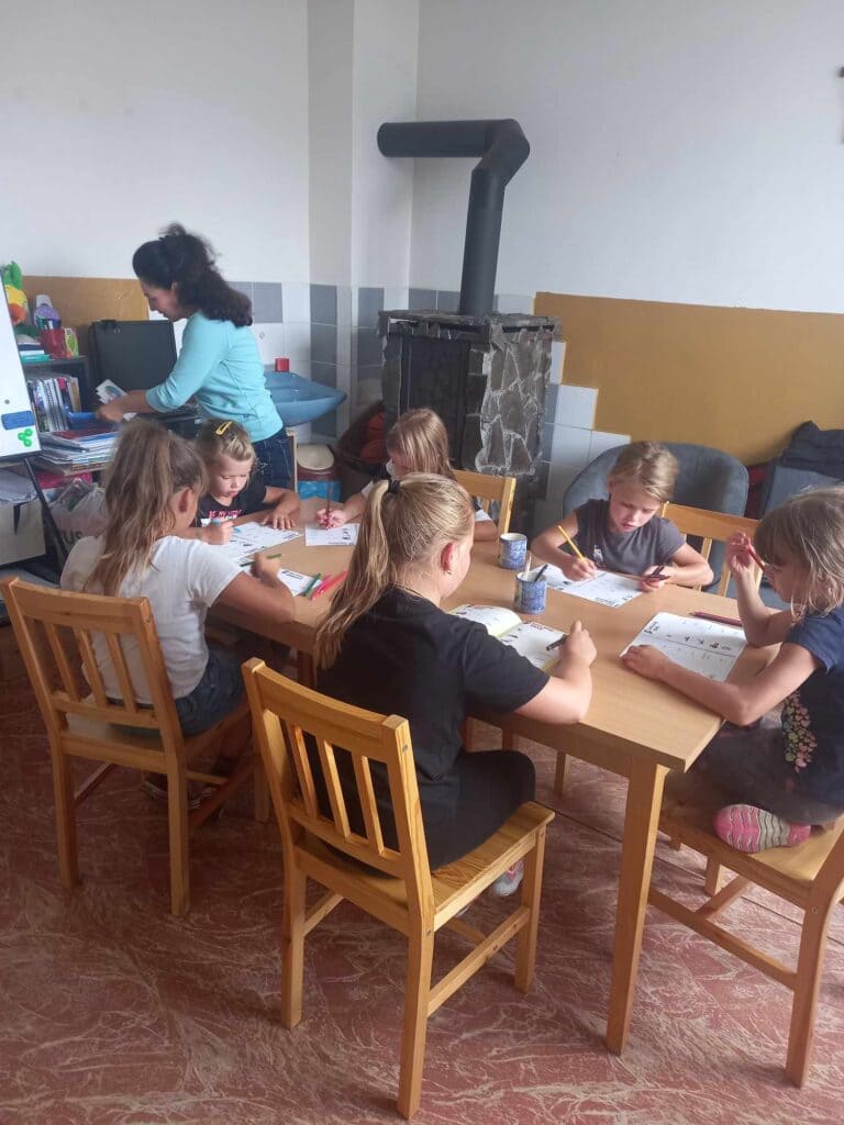 skupinka detí kreslí pri stole
